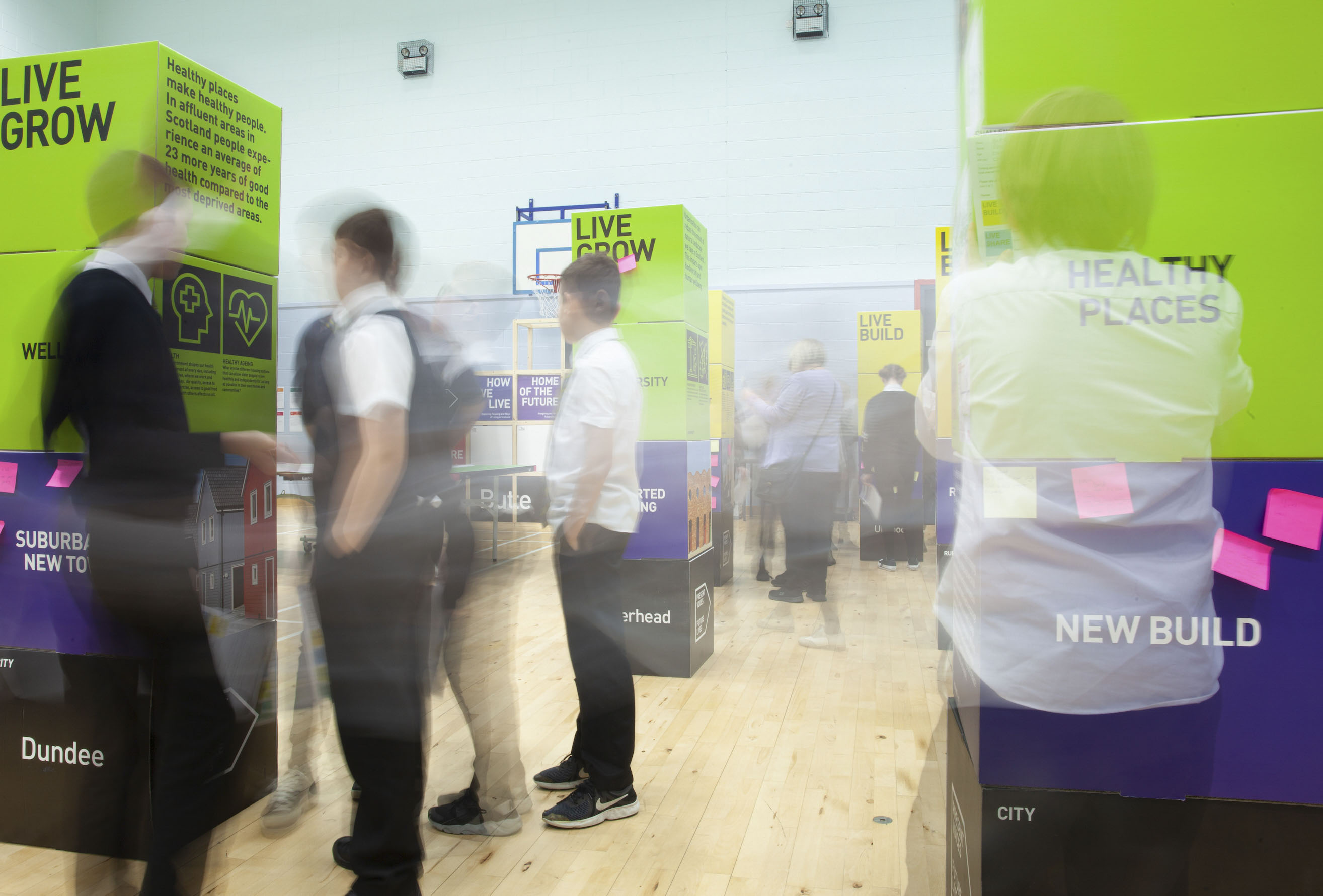 An exhibition of green and purple blocks with text on them with blurred outlines of school pupils exploring the exhibition.