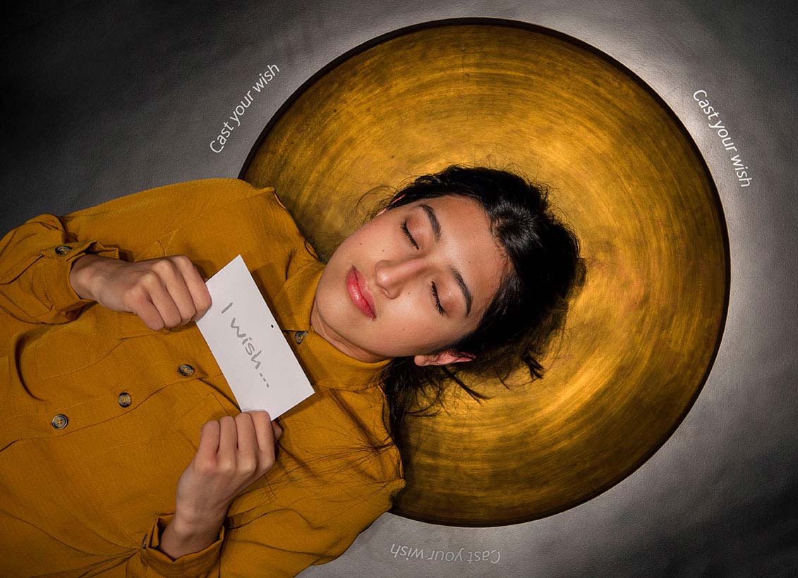 A young woman with her head laying on a copper disk and holding a card with the words 'I wish...'