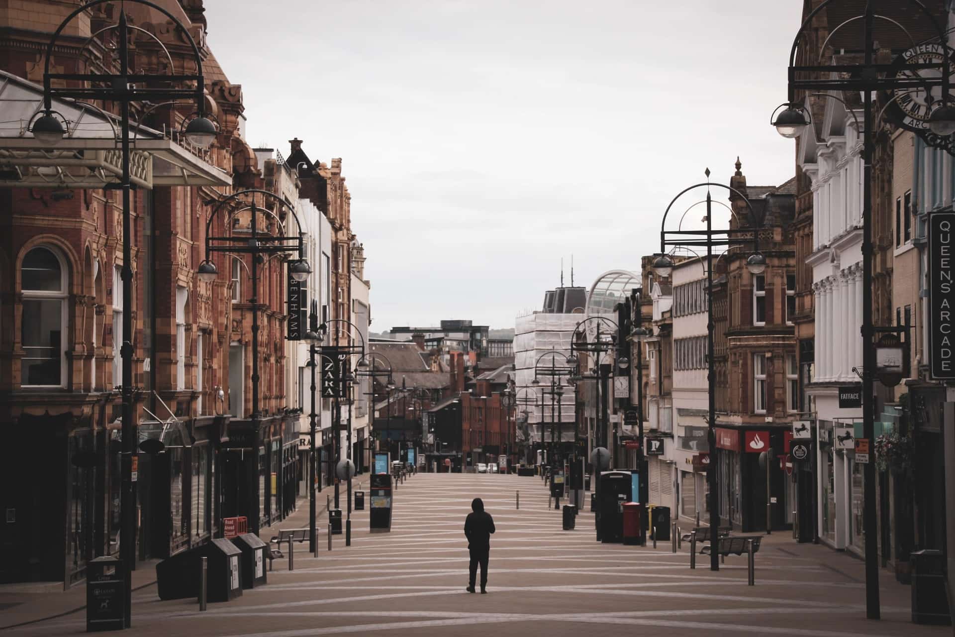 A person wearing a black hoodie walks on an empty high street.