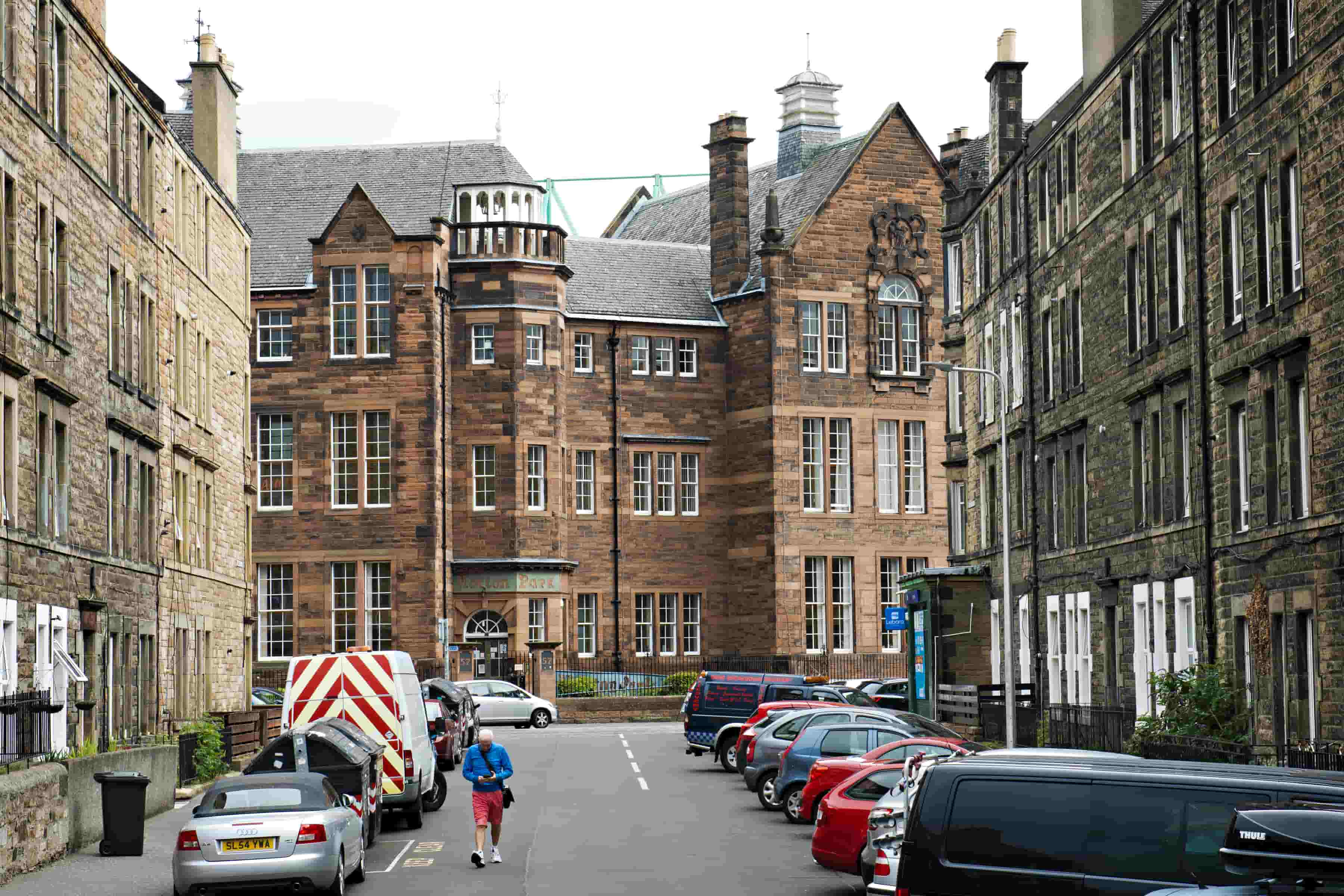 A man in a blue jacket walks down a street in between a row of building.