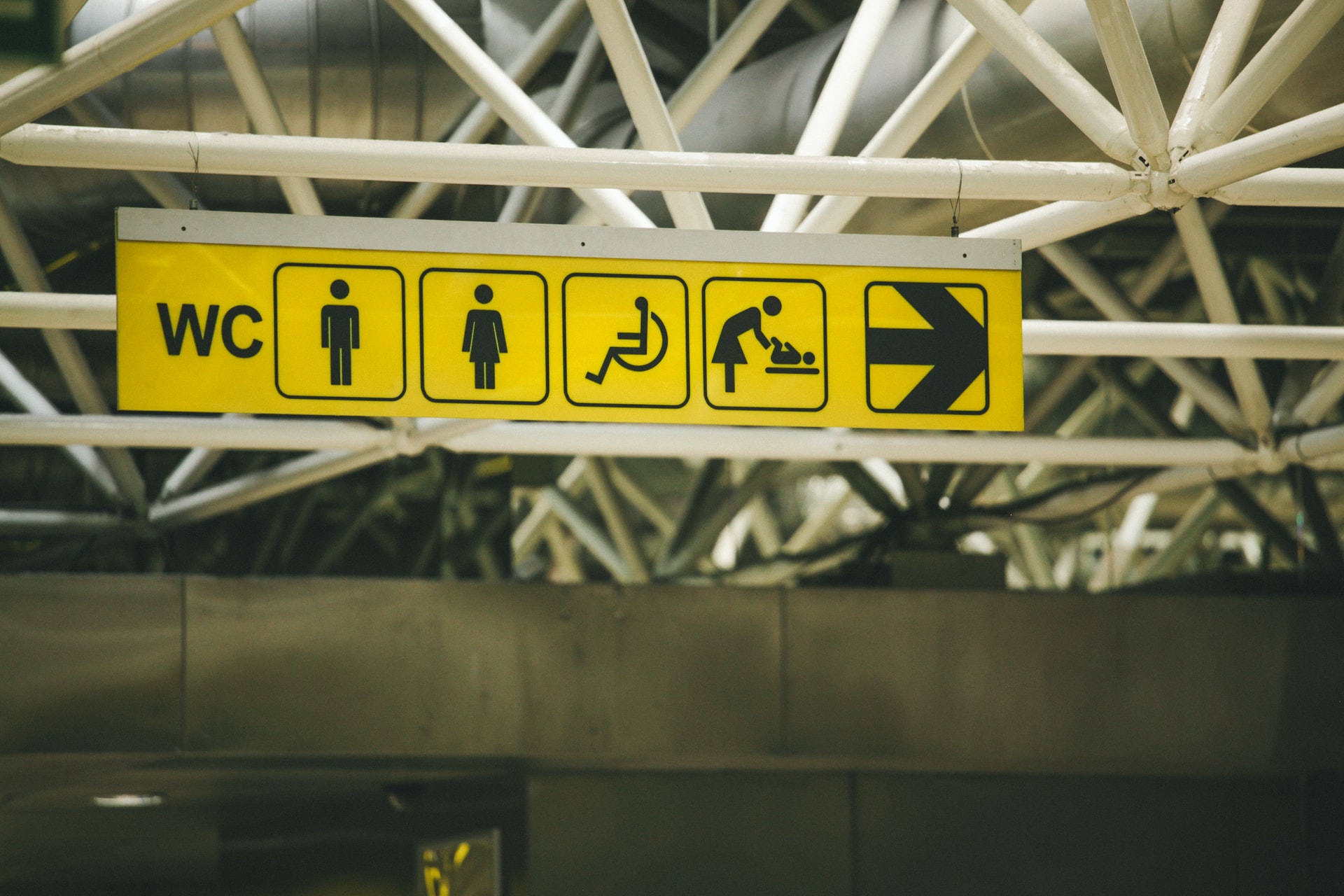 A photograph of a yellow toilet signs in an airport.