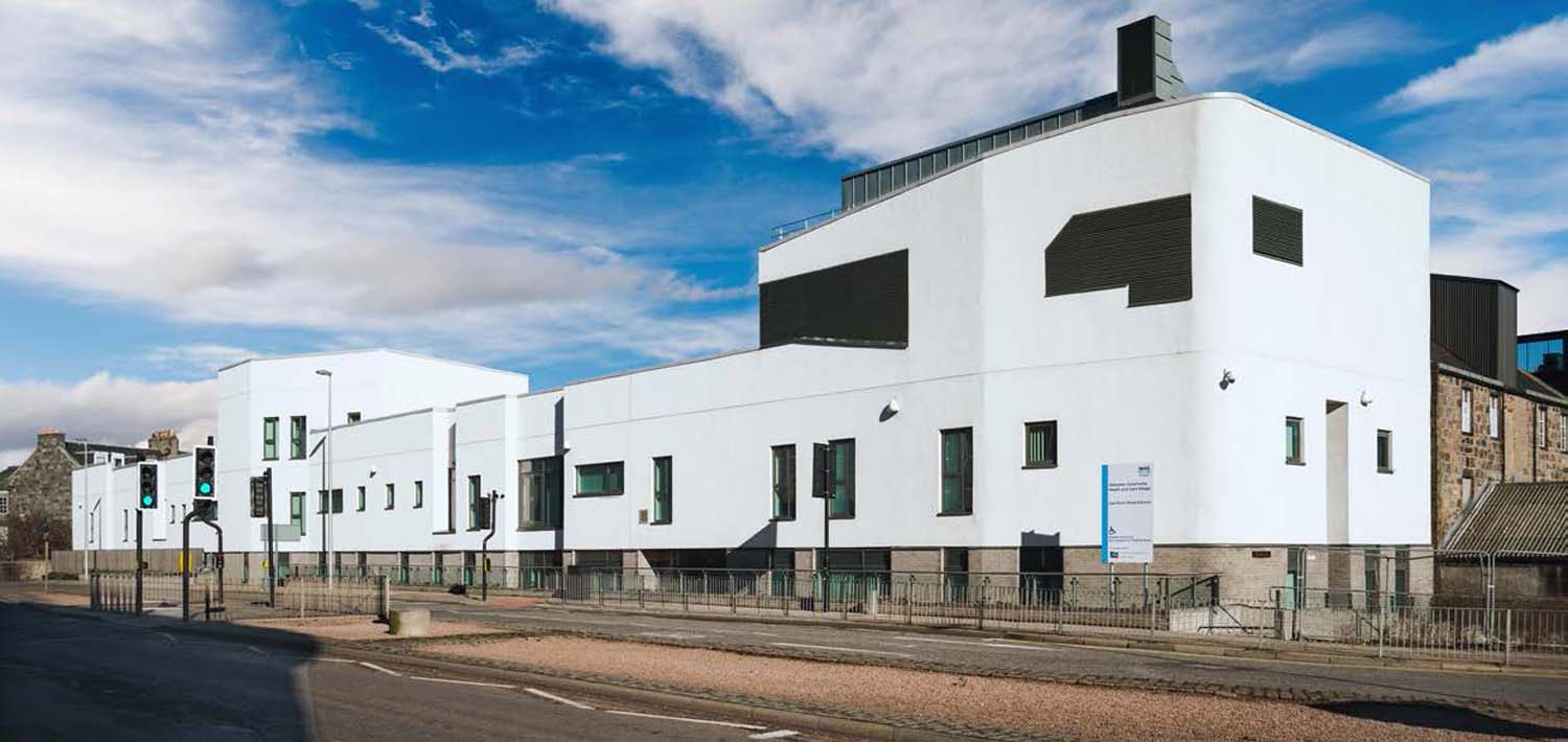 A street view of Aberdeen Community Health and Care Village's white façade, set against a bright blue sky.
