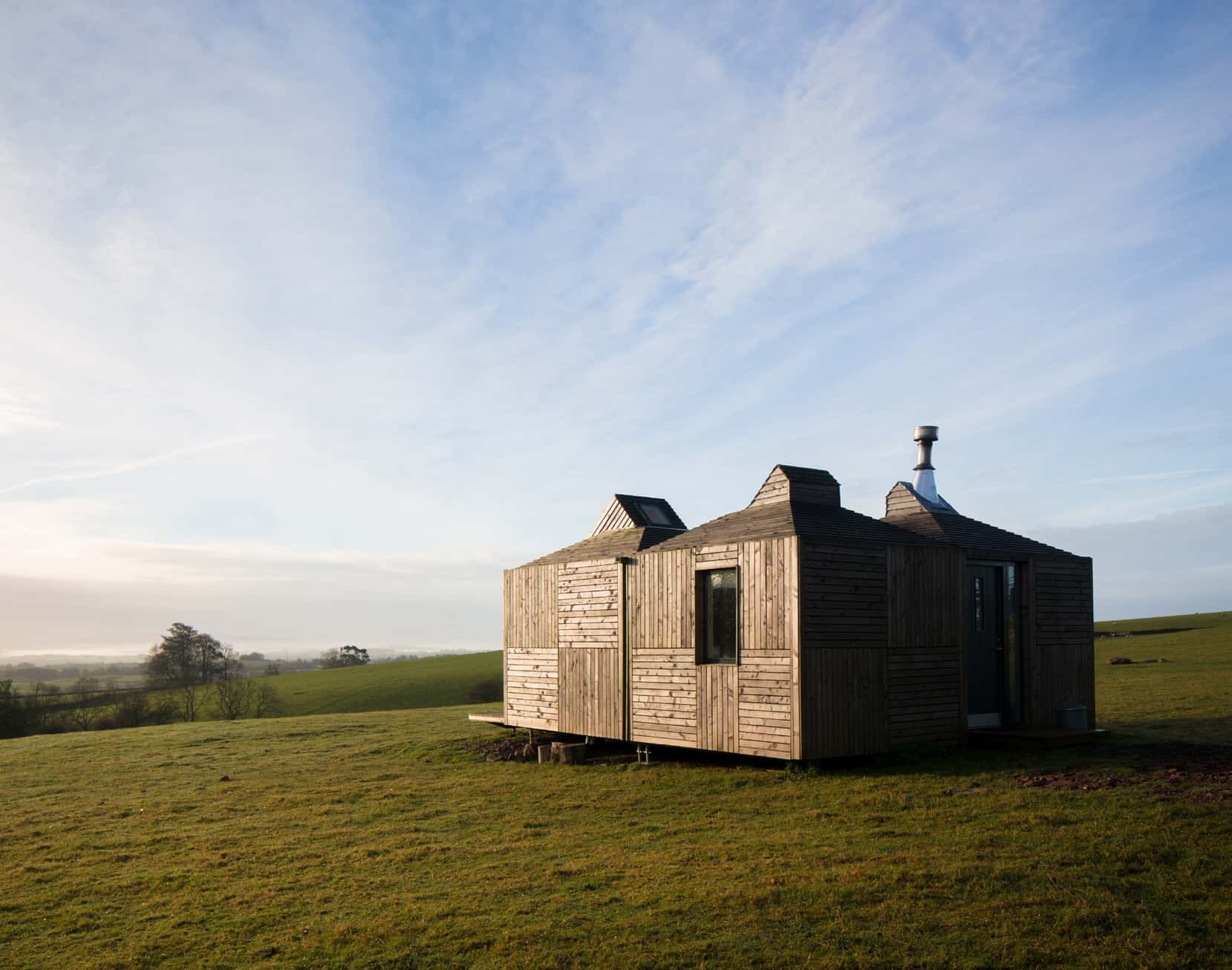 A small wooden façade building overlooking a rural setting. The building's wooden façade has a dark greying colour.