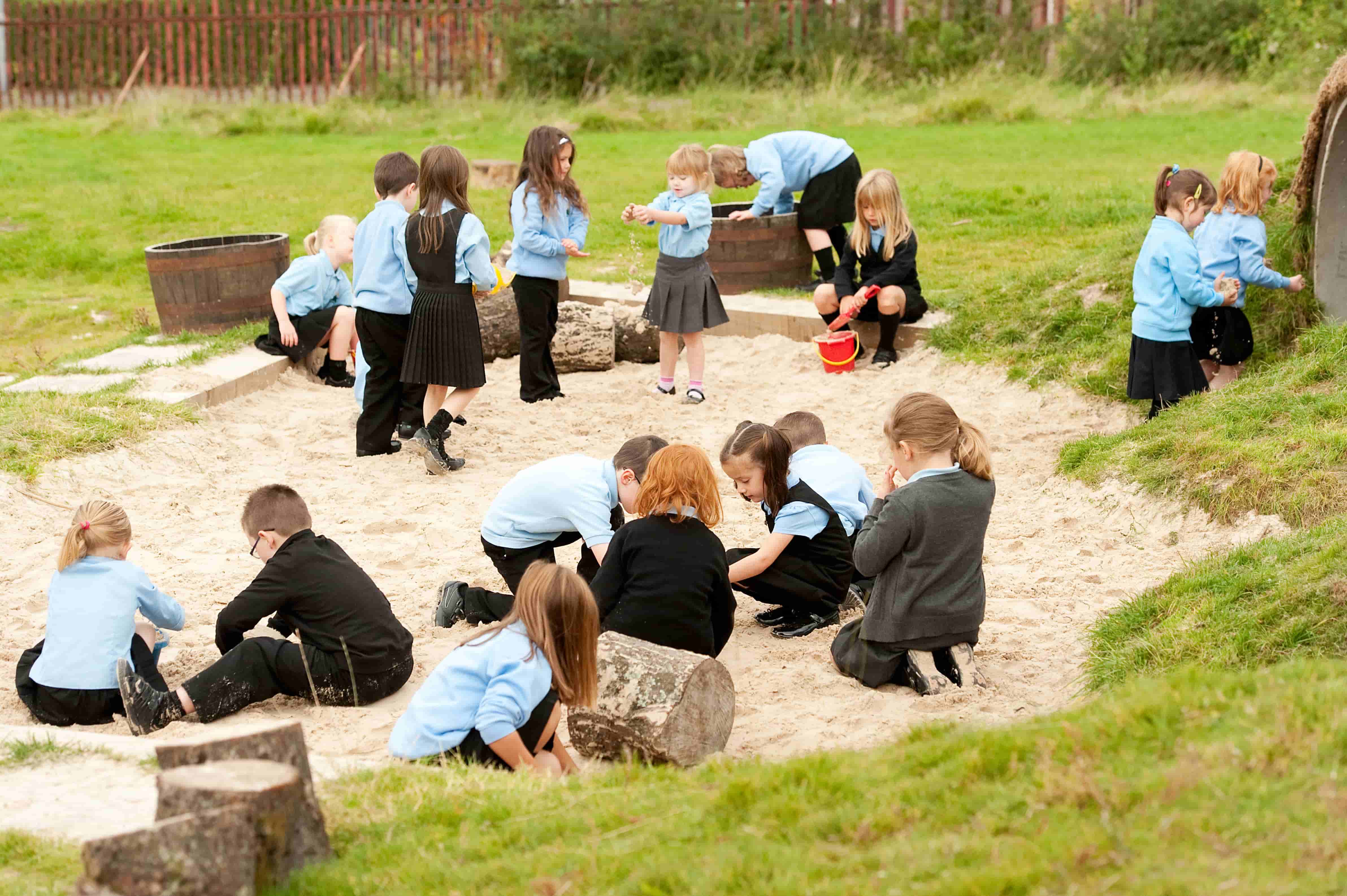 Children wearing school uniform playing in the sand surrounded by grass.