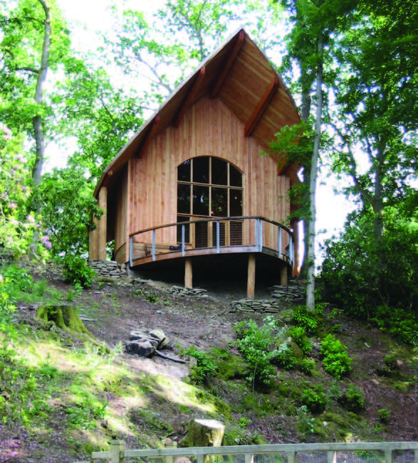 A wooden building set into a hill surrounded by trees with a bow shaped viewing balcony