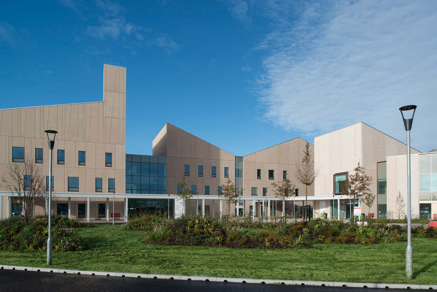 A photograph of the entrance to Dumfries and Galloway hospital - the roof line is made of triangular shapes, and the building is made of light coloured stone. 
