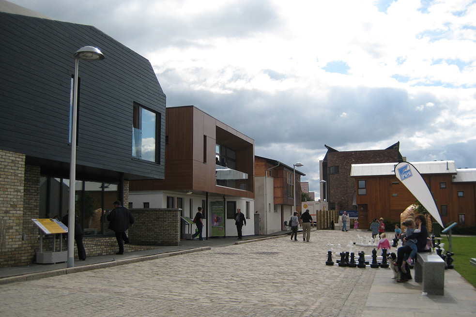 A house overlooking a street and neighbourhood green, with about ten people in the street.