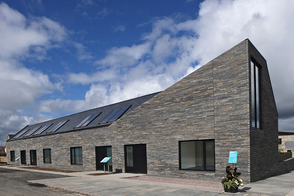 A long, modern house with a distinctive raised corner and large windows on a partly cloudy day.