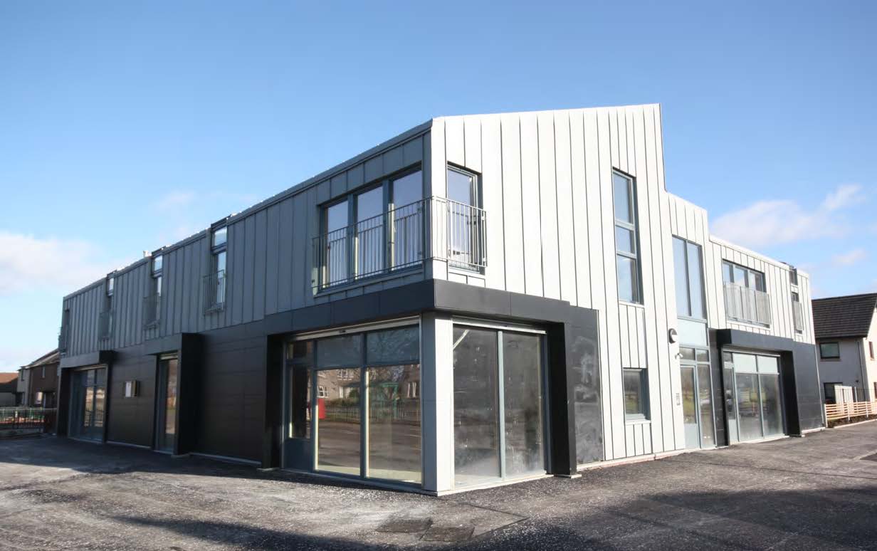 A photograph of the corner of a metal clad two-storey building which sits on a street and has a black shopfront on the corner 
