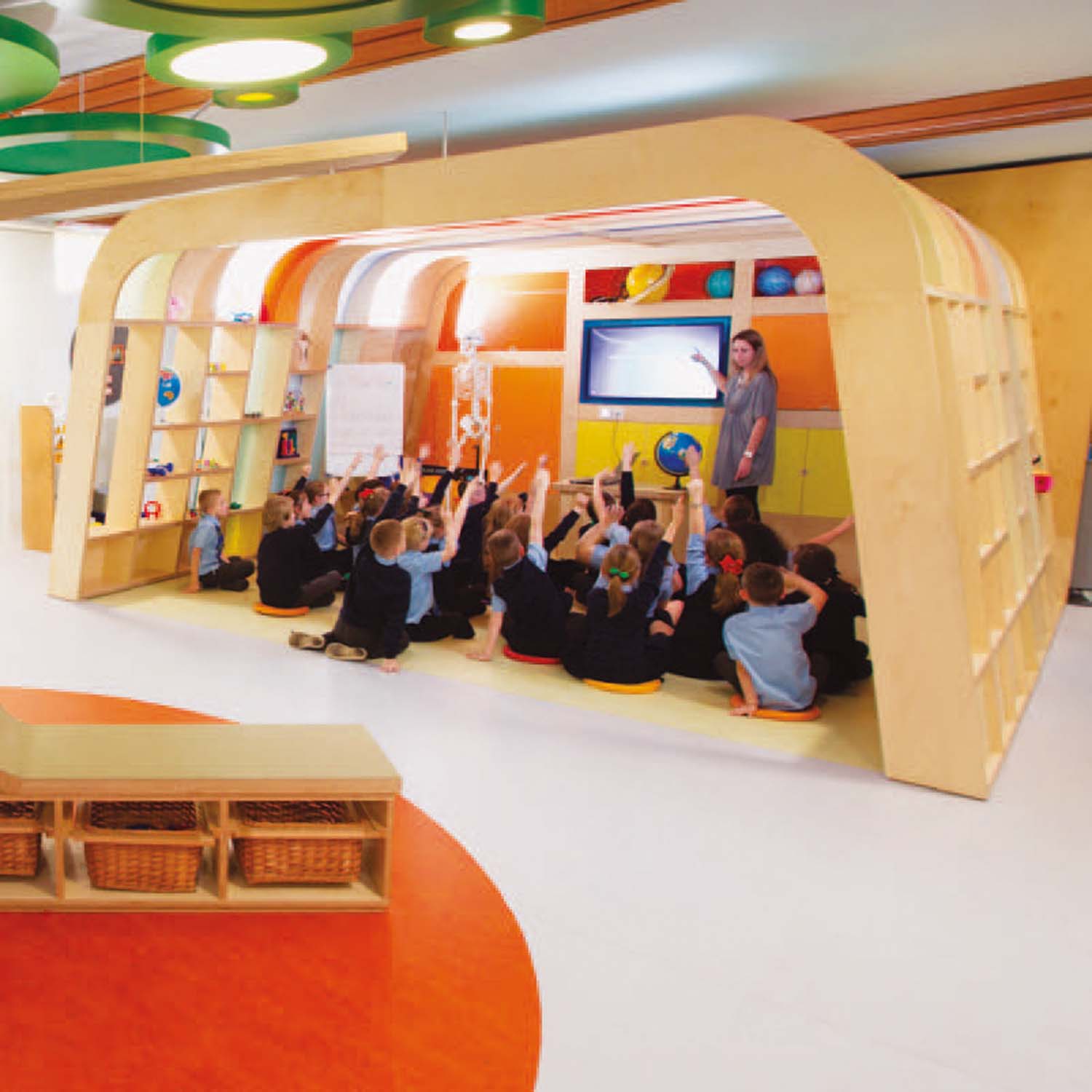 A wooden structure inside a school where primary school pupils sit on the floor as part of a lesson. 