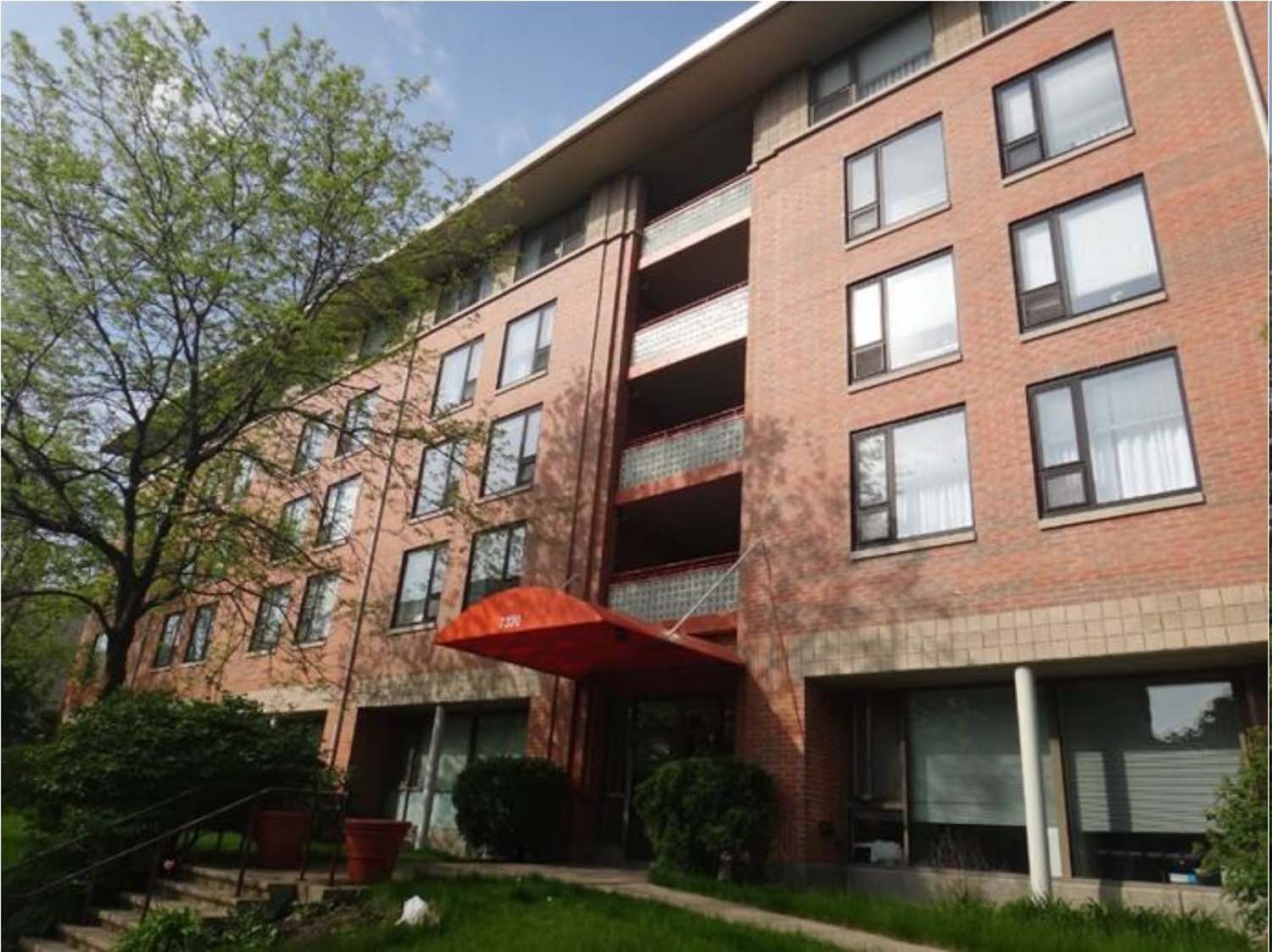 A five-storey apartment building in Chicago, Illinois, made of brick, has a bright red canopy entrance.