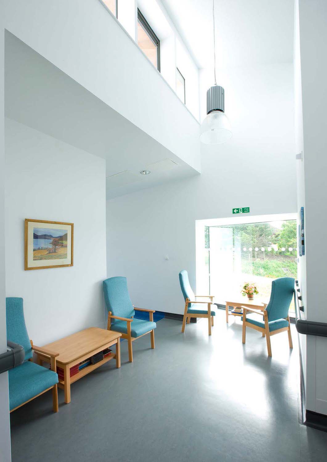 A seating area at the end of a corridor. It is lit by natural light from a large window on one side and clerestory windows on the other.