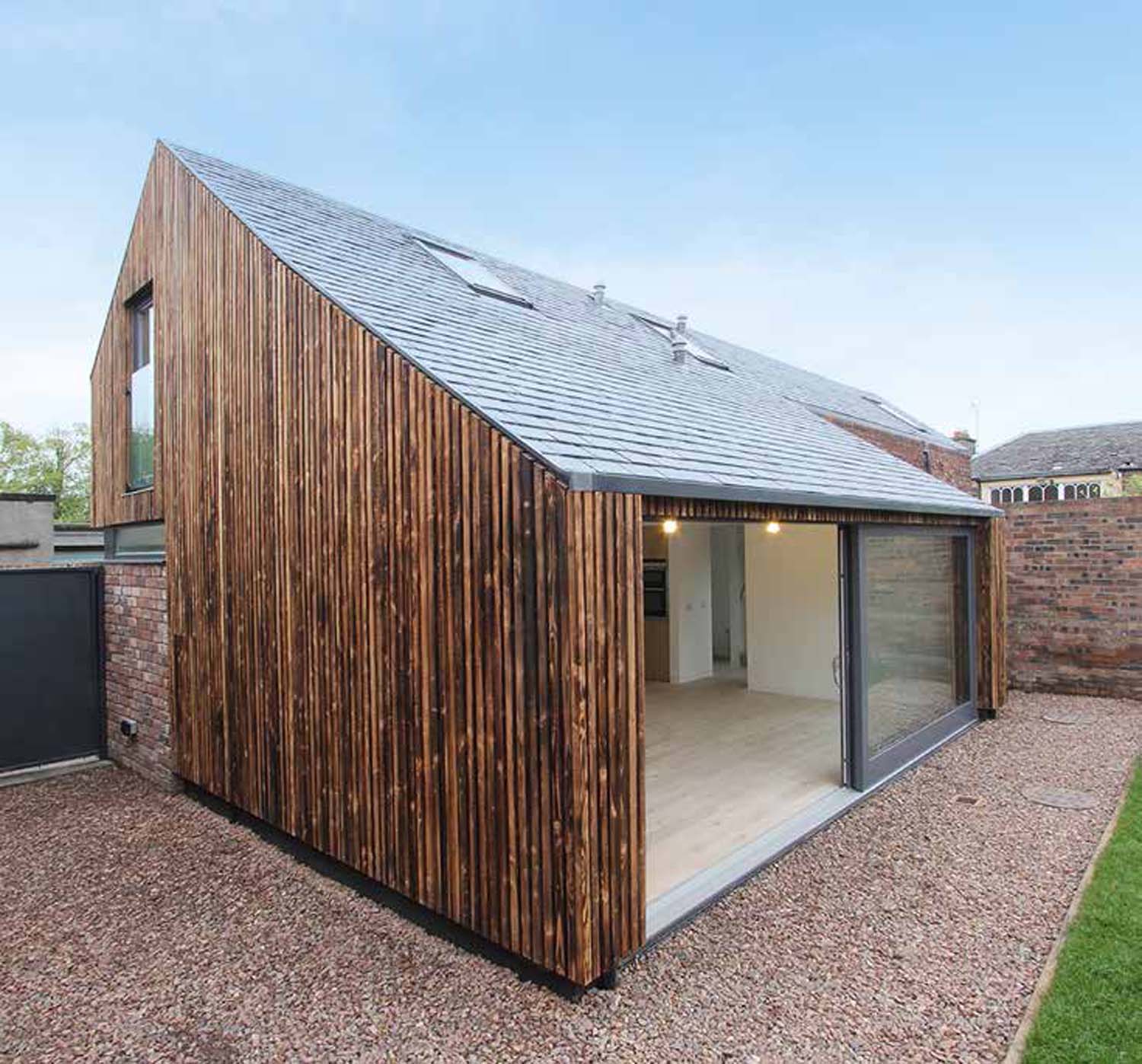 A corner view of the house on Rosefield Avenue Lane. Vertical timber slats cover the side of the wall with the sliding door wide open.