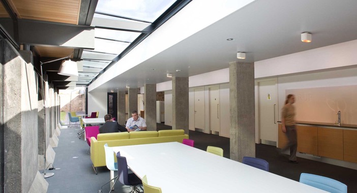 Black framed skylights light up a social space at Scotstoun House as two people sit and have a meeting.