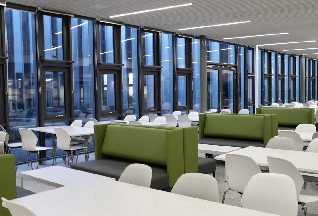 Tables, chairs and padded seating spaced evenly Forth Valley College refectory. The tables and chairs are white, and the seating booths are olive green.