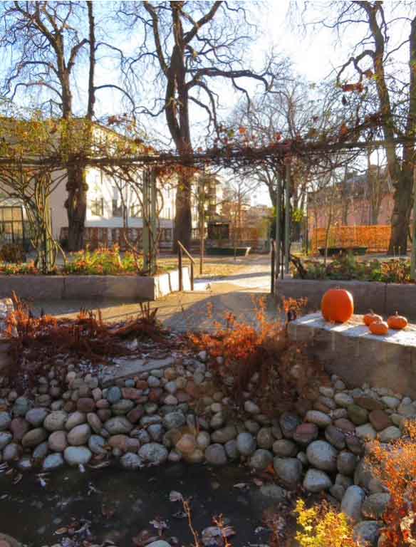 An outdoor folly in a autumnal garden which includes seating area and a display of orange pumpkins