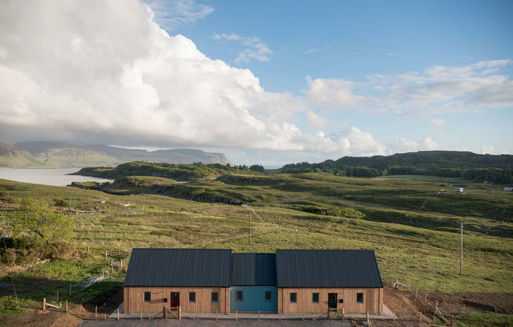 Two single-story attached houses with grey coloured roofs and timber facades, set against a rural landscape on Ulva island. 