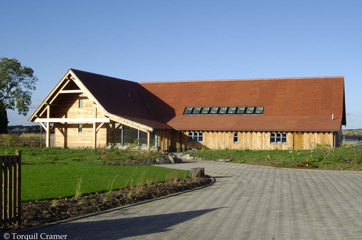 A stone driveway leads to a larch wood cladding façade long building in a rural setting.