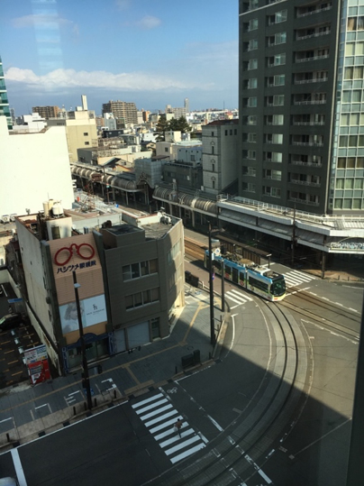 A blue and white tram drives past a junction in Toyama.