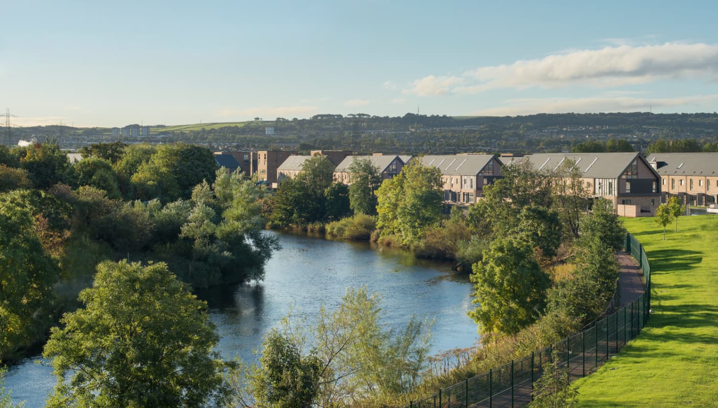A photograph of a housing development next to a river bordered by green trees
