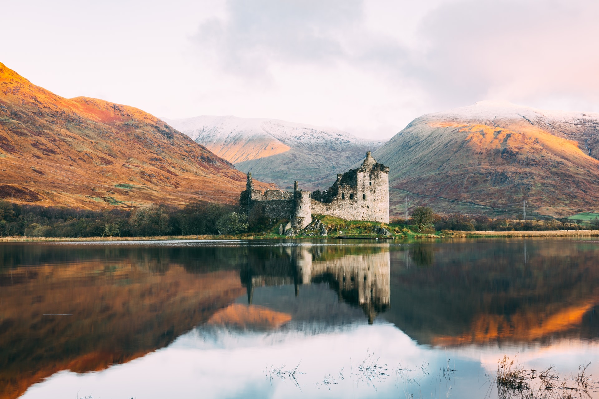 Kilchurn Castle flanked by two mountains with its reflection in the still lake.