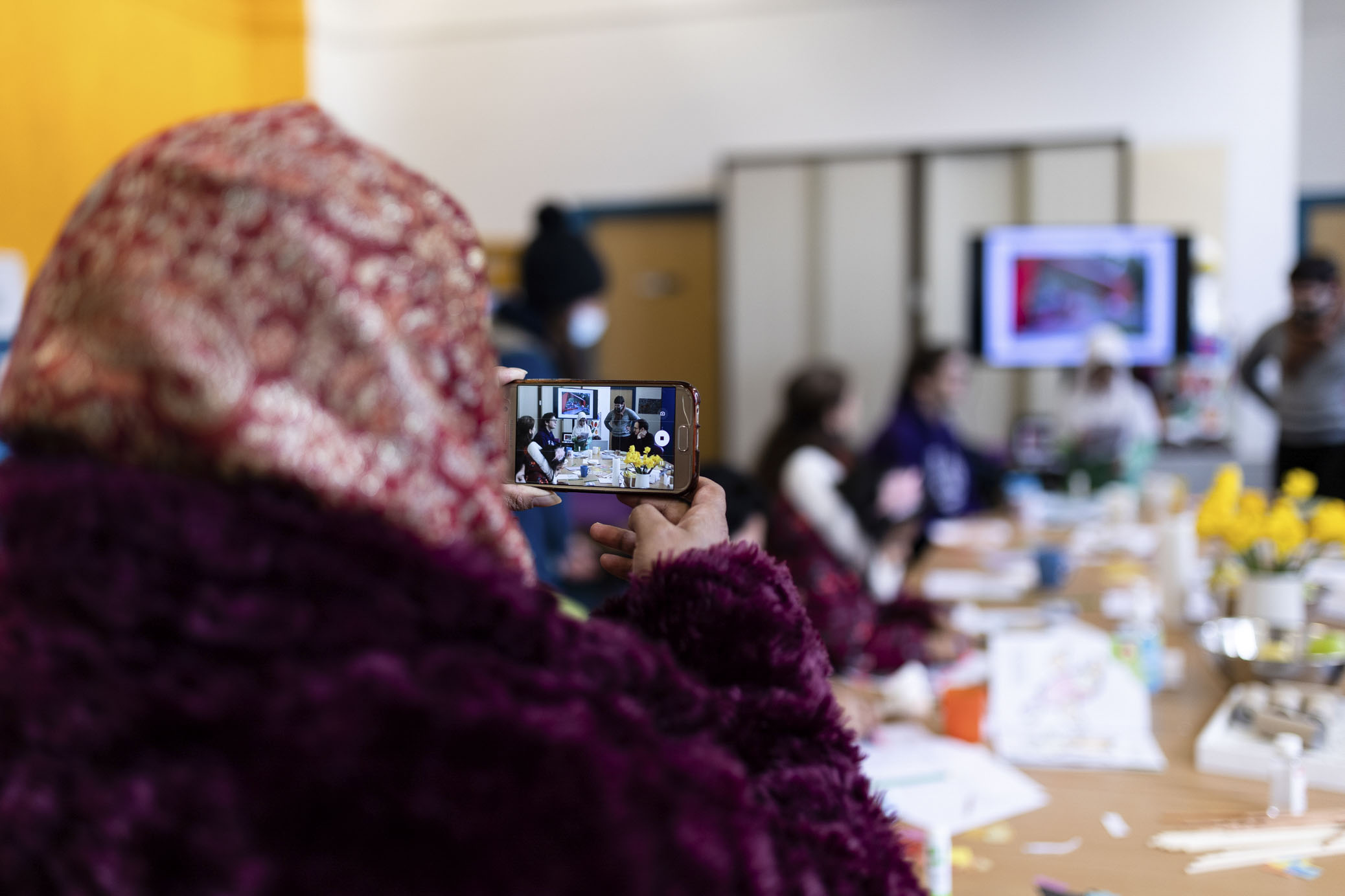 A woman wearing a hijab is taking a photograph of a group of people having a workshop.