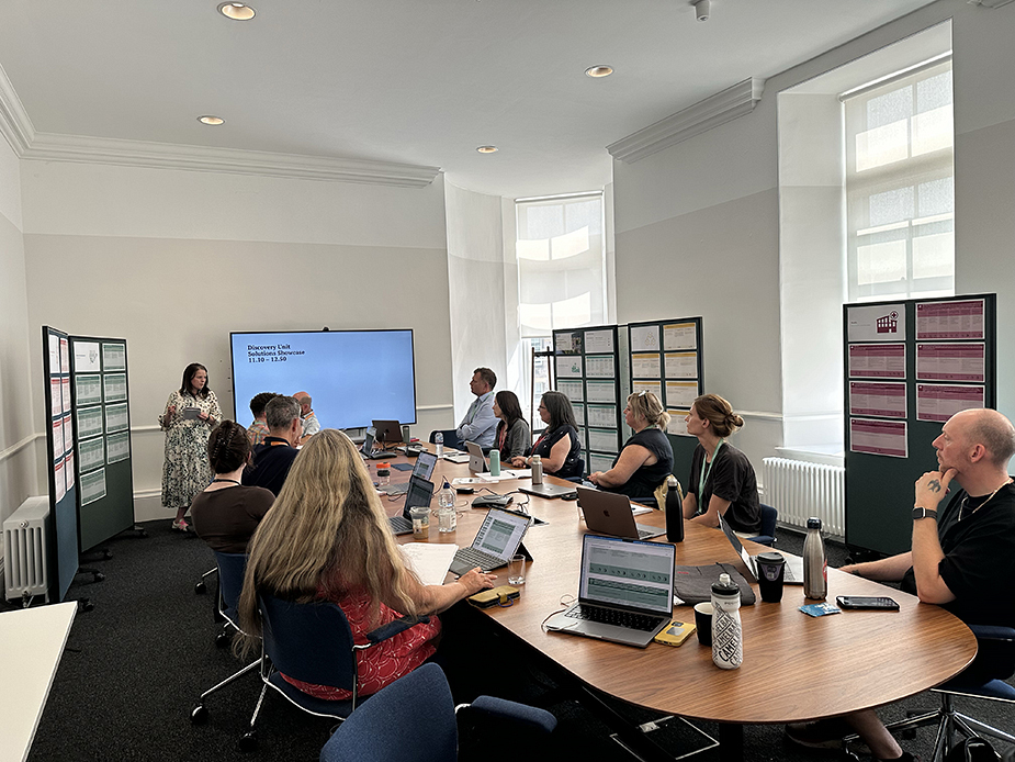 People sat in a meeting room surrounded by boards with images and texts.